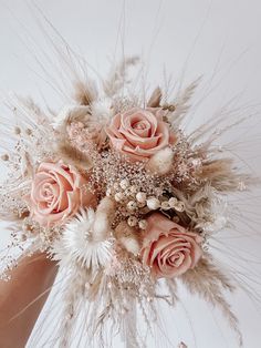 a bridal bouquet with pink roses and feathers in someone's hand on a white background