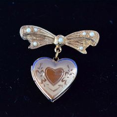 "This is a beautiful vintage hand engraved gold heart locket pin. The 14KT gold filled heart is hanging on a bow which has seven pearls mounted on it. Open the heart and there are places to hold two photographs. It is marked on the back of the heart \"14KT GF R\". The locket comes in its original grey velvet clamshell box with red and gold metallic sticker marked \"14KT GOLD FILLED HAND ENGRAVED\". Condition: Excellent vintage condition. It does not look like it has ever been removed from box. S Heirloom Engraved Brooches For Gifts, Elegant Locket Brooches For Gift, Antique Heart Brooch For Wedding, Antique Heart-shaped Wedding Brooch, Gold Locket Brooches For Gifts, Antique Gold Jewelry With Heart Charm For Wedding, Antique Gold Wedding Jewelry With Heart Charm, Vintage Heart-shaped Brooch Jewelry, Antique Heart-shaped Brooch For Gift