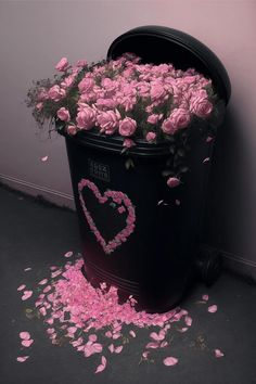 a trash can filled with pink flowers next to a wall and floor covered in petals