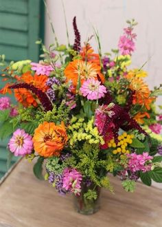 a vase filled with lots of colorful flowers on top of a wooden table next to a green door