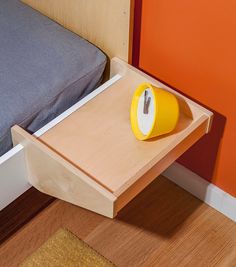 a yellow alarm clock sitting on top of a wooden table next to a blue bed