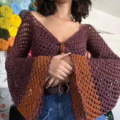 a woman standing in front of a wall with crocheted shawls on it