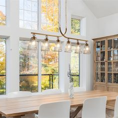 a large dining room table with white chairs and lights hanging from it's ceiling