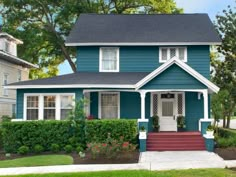 a blue house with white trim and red steps in the front yard, surrounded by greenery