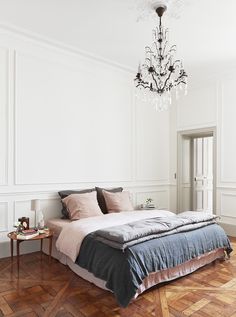 a bed sitting on top of a wooden floor next to a chandelier