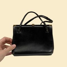 "Vintage Jana top strap black leather handbag, manufactured c. 1950s-1960s. Features brass hardware, a sturdy frame, a brown coin pocket attached by a cord, one main compartment, a small zip up pocket, and an open pocket flap.    - Brand: Jana    - Size: 8\" x 6\" x 3\"    - Time Period: c. 1950s-1960s    - Color(s): Black and brass exterior; brown interior    - Materials: Leather    - Made in: Not listed    - Condition: In fair, vintage condition. Straps are cracked, exterior has scratches and Vintage Formal Satchel With Metal Hardware, Vintage Shoulder Bag With Metal Hardware For Office, Vintage Office Shoulder Bag With Metal Hardware, Vintage Office Satchel With Detachable Strap, Vintage Office Bags With Brass Hardware, Retro Evening Bag With Brass Hardware, Vintage Formal Bag With Brass Hardware, Retro Evening Bags With Brass Hardware, Vintage Black Shoulder Bag With Metal Hardware