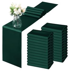 a vase with flowers is sitting on top of a stack of green table runners next to each other