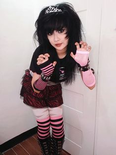 a woman with black hair and pink gloves posing for the camera in front of a door