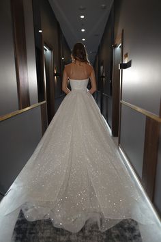 a woman in a wedding dress is walking down the hall with her back to the camera