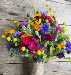 a vase filled with lots of colorful flowers on top of a wooden table next to a wall