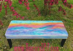 a painted bench sitting in the grass near flowers