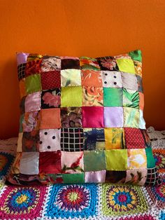 a multicolored patchwork pillow sitting on top of a crocheted blanket