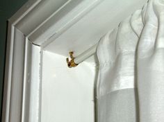 the corner of a white curtain with a gold hook on it's end, in front of a window