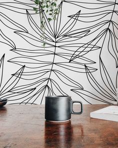 a coffee cup sitting on top of a wooden table next to a plant in a vase