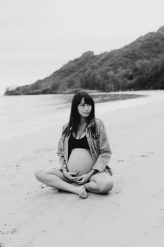 a pregnant woman is sitting on the beach with her belly in her hands and looking at the camera