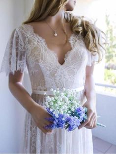 a woman in a white dress holding a blue and white bridal bouquet with flowers