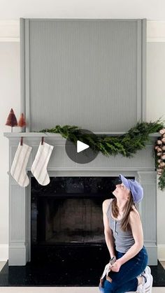 a woman sitting on the floor in front of a fireplace with stockings hanging from it