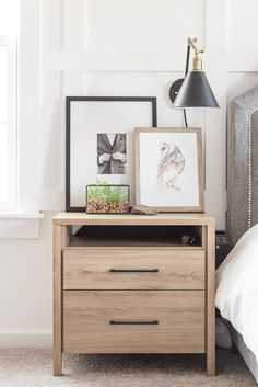 a nightstand with two pictures on it next to a lamp and a framed bird print