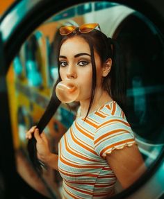 a woman with long hair and sunglasses blowing bubbles in front of a mirror