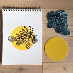 a spiral notebook sitting on top of a wooden table next to a yellow circle and a blue piece of paper