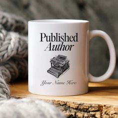 a white coffee mug sitting on top of a wooden table next to a pile of yarn