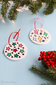 two christmas ornaments hanging from a tree on a blue surface with red berries and greenery