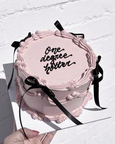 a pink cake with black lettering on it and ribbon around the edges is being held up by someone's hand