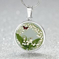 This May Birth flower Necklace features a delicate and beautiful butterfly charm, paired with the delicate and elegant Lily of the Valley flower, the birth flower for the month of May. Created with our patent-pending design, this necklace is made of high quality surgical steel with the option of an 18k gold finish for added luxury. This necklace is the perfect keepsake for yourself or a loved one, and can be customized with a special photo of your choice. You can also opt for custom engraving on Silver Necklace With Flower Charm For Spring, Silver Necklaces With Flower Charm For Spring, Silver Necklace For Spring Gift, Silver Necklaces For Spring Gift, Spring Gift Silver Necklace, Elegant Spring Butterfly Jewelry, Dainty Silver Butterfly Necklace For Wedding, Elegant Green Butterfly Necklace As Gift, Elegant Green Butterfly Necklace For Gift