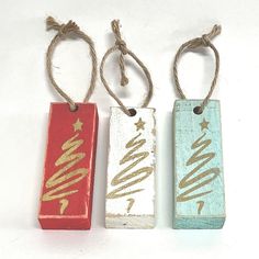 three small wooden tags with gold lettering on them hanging from twine strings, one red and one blue