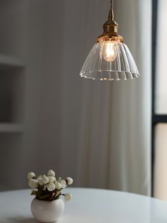 a white vase with flowers sitting on top of a table next to a light fixture