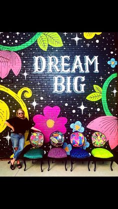 a woman sitting in front of a sign that says dream big with flowers on it