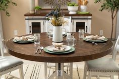 a dining room table set with place settings and flowers in a vase on the centerpiece