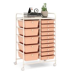 a white cart with many pink drawers on top of it next to a potted plant