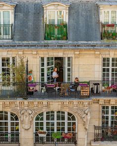 two people sitting on the balcony of an apartment building with potted plants and flower boxes