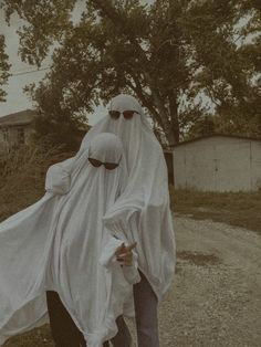 two people dressed in white walking down a dirt road next to a tree and building