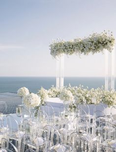 an outdoor wedding setup with clear chairs and white flowers