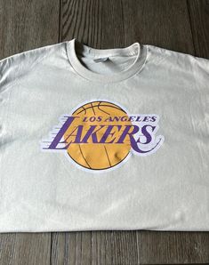 the los angeles lakers t - shirt is laying on top of a wooden floor with it's logo