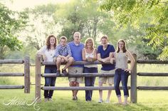 a group of people standing next to each other on top of a wooden bench in front of a fence