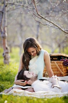 a woman sitting on the ground next to a man who is holding a basket with grapes in it