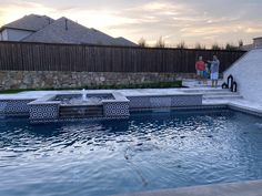 two people standing on steps near a pool in the middle of a backyard with water