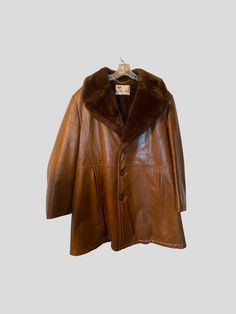 Vintage circa 1980s brown leather rancher style coat by Lakeland. Size 42.  Leather outer with soft faux wool lining.  Single back vent.  This coat has some weight to it and should be quite warm.  In good vintage condition with no rips, holes, tears or stains. Lining is well attached and buttons open and close smoothly. Please note this is a Vintage item and may show signs of wear such a slight surface ware.  There is slight scuffing on one of the buttons. Please see photos.   Approximate measur Retro Brown Outerwear For Cold Weather, Retro Leather Outerwear For Winter, Brown Leather Fur Coat For Fall, Vintage Leather Jacket For Winter, Classic Brown Outerwear With Faux Fur Lining, Retro Leather Winter Outerwear, Retro Brown Leather Jacket For Winter, Vintage Leather Jacket For Cold Weather, Retro Brown Fur Coat For Fall