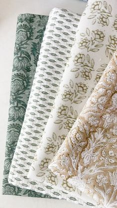 four different colors of fabric sitting on top of a white tablecloth covered in green and brown designs