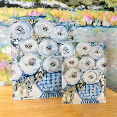 two blue and white vases with flowers in them sitting on a table next to each other