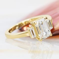 an emerald cut diamond ring sitting on top of a pink flower