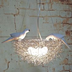 two white birds sitting on top of a bird nest hanging from a ceiling light fixture