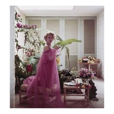 a woman in a pink dress standing next to a plant