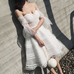 a woman in a white dress leaning against a wall