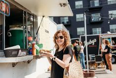 a woman standing in front of a food truck holding a plate of food and smiling at the camera