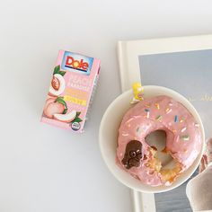 a pink doughnut sitting on top of a white plate next to a box of dole