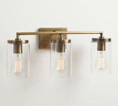 three light fixtures mounted on a wall with clear glass shades and brass fittings,